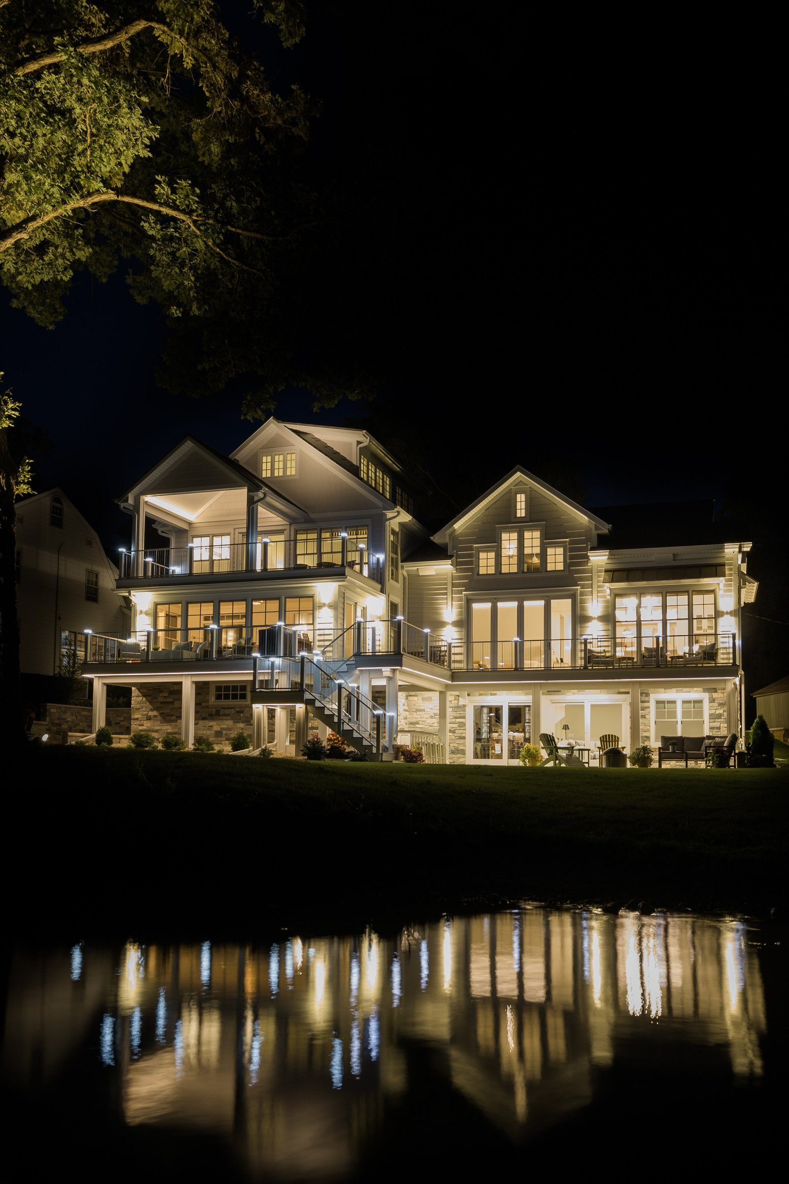 Night view of the lit Burlington lakehouse from the shoreline, its lights reflected in the dark water