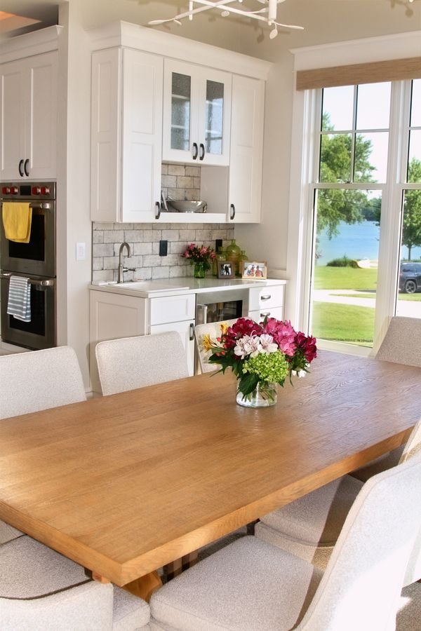Wood dining table with fresh flowers, white custom cabinetry, and the lake visible through the window