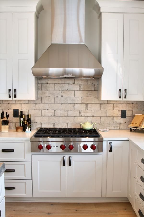 Professional range with a custom stainless hood, brick backsplash, and white shaker cabinetry