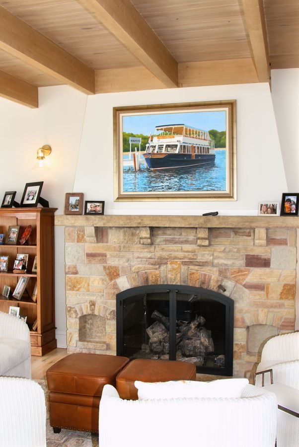Great room with a natural stone fireplace, exposed beam ceiling, and a painting of a lake excursion boat above the mantel