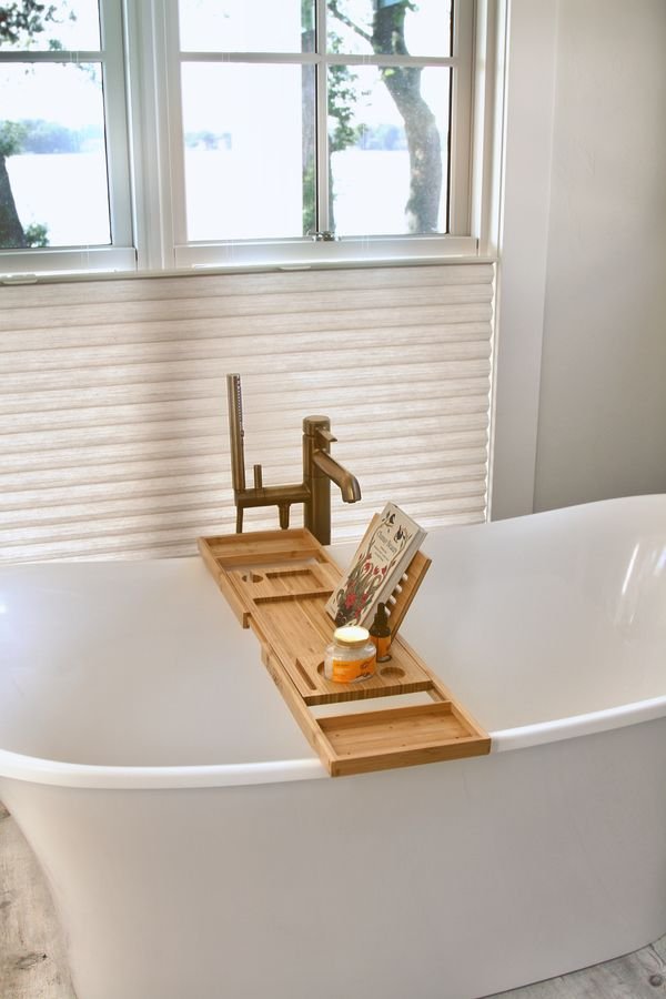 Freestanding soaking tub with a brass floor-mounted filler beneath windows facing the lake