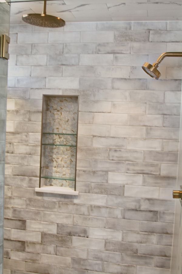 Tiled shower with a rain head, a brass shower head, and a recessed mosaic niche