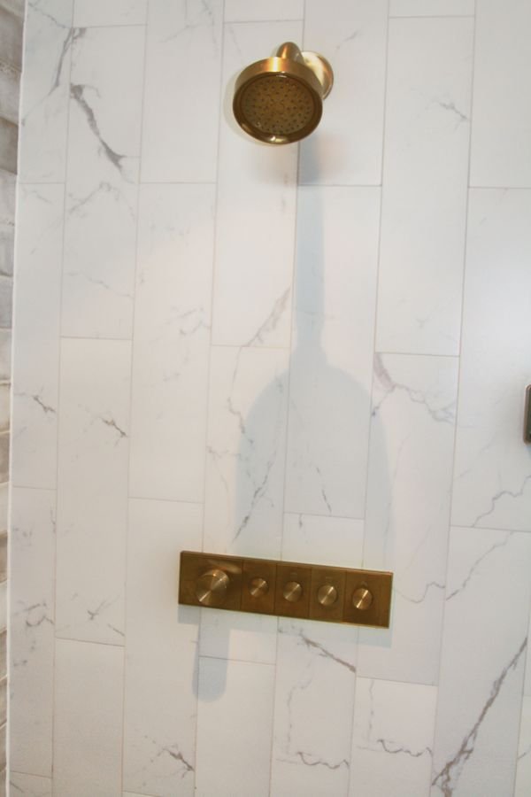 Brass shower head and control panel on large-format marble-look tile