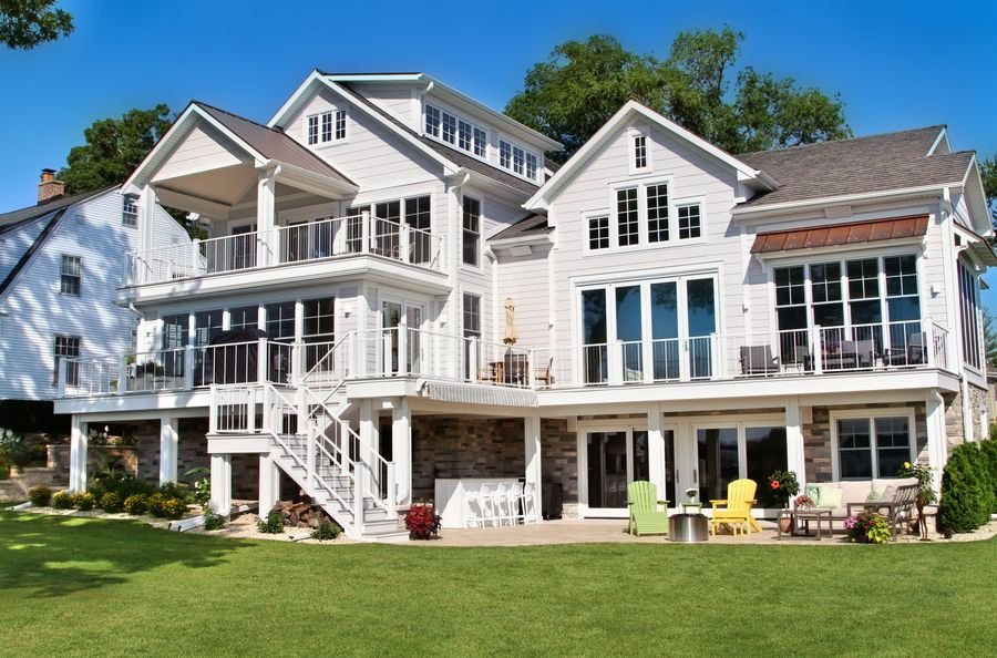 Full lakeside elevation of the home: three levels of white siding, decks, and porches above a stone walkout level and patio