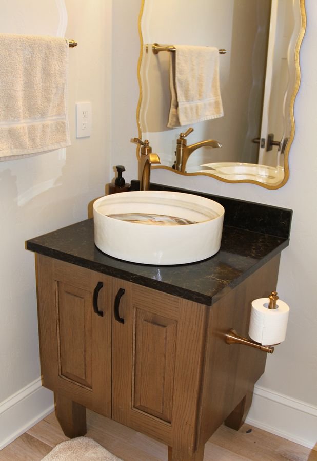 Powder room with a vessel sink on a dark stone top, a wood vanity, and a wavy gilt mirror