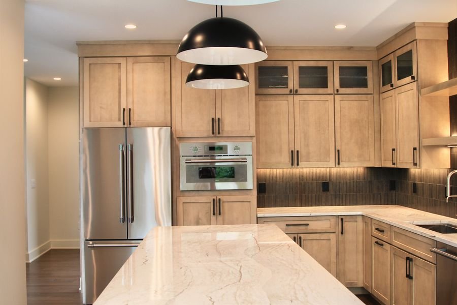 Kitchen island facing the refrigerator, wall oven, and maple cabinetry with reeded glass uppers