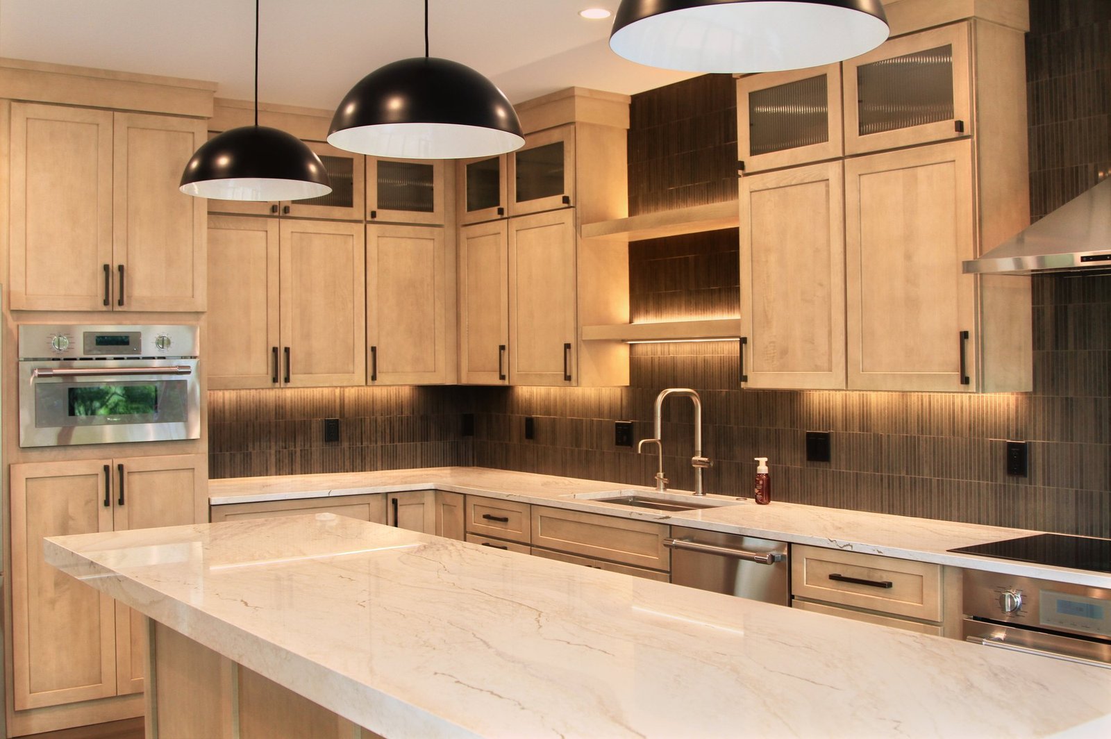 Kitchen of the Whitewater lakehouse: a long stone island under black dome pendants and maple cabinetry