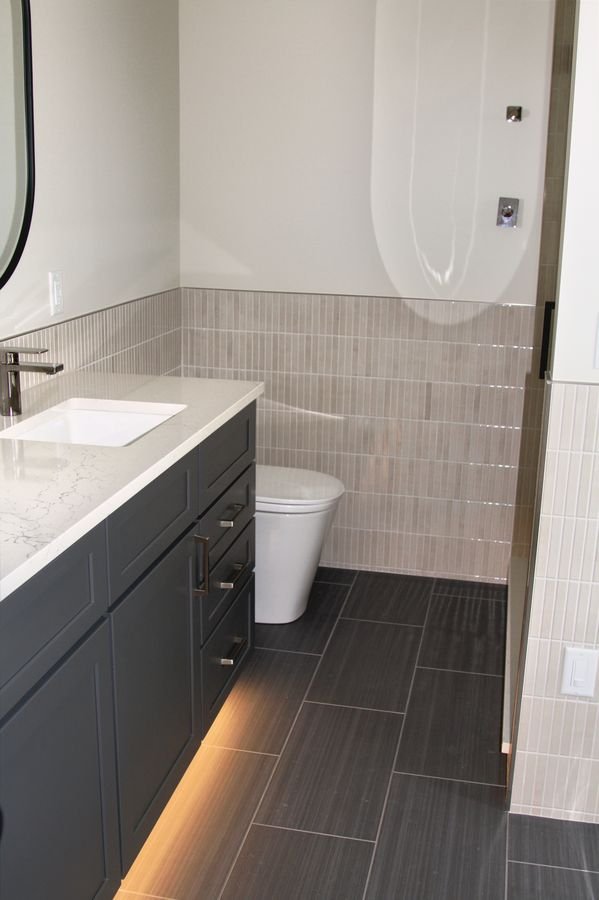 Bathroom with a dark floating vanity lit from beneath, a stone countertop, and tiled walls