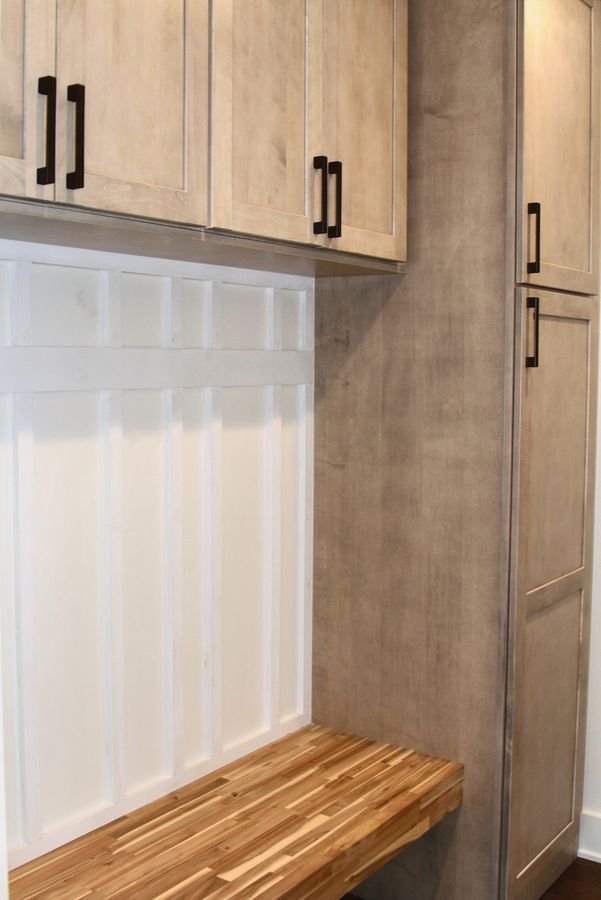 Butcher block bench beneath white board and batten, with maple cabinets above and a tall cabinet beside