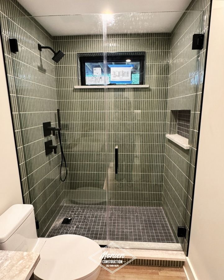 Walk-in shower in sage green vertical tile with black fixtures, a glass door, and a small window